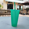 A bright green glitter party cup with a straw is placed on a white table outdoors.