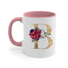 A pink ceramic coffee mug featuring a large gold letter B decorated with floral accents.