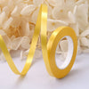 A roll of golden satin balloon ribbon unwinding against a background of white flowers.