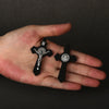 A hand holds a set of black wooden St. Benedict crucifix pendants.