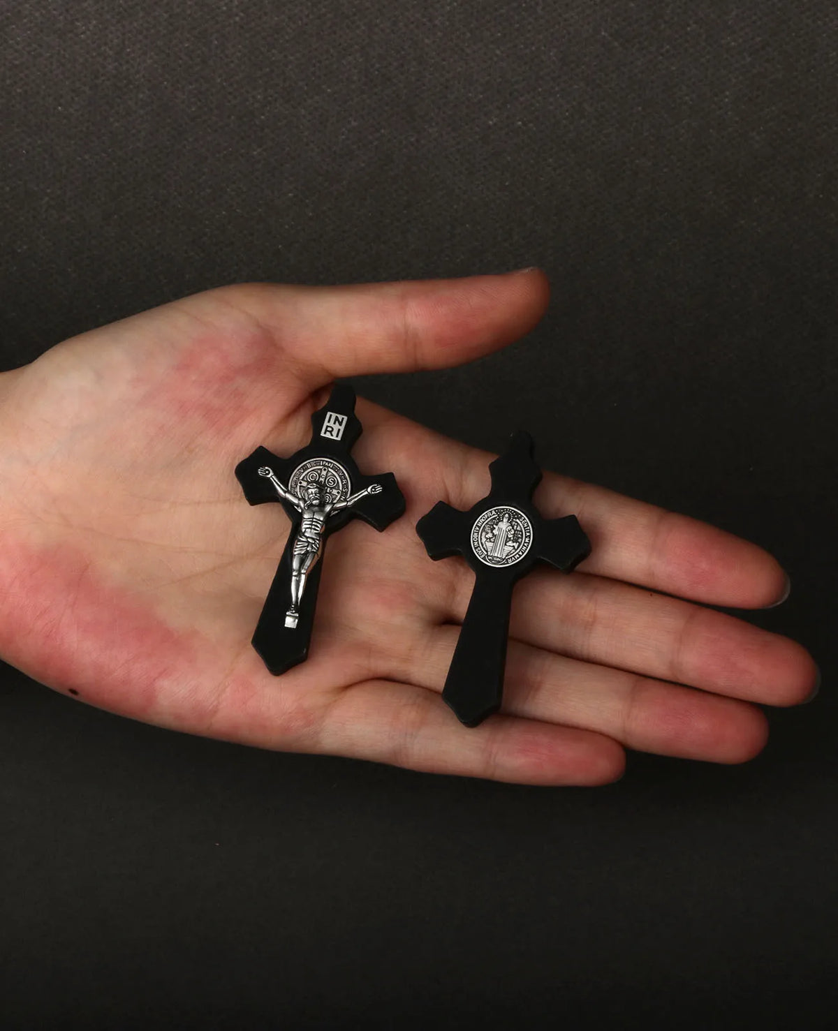 A hand holds a set of black wooden St. Benedict crucifix pendants.