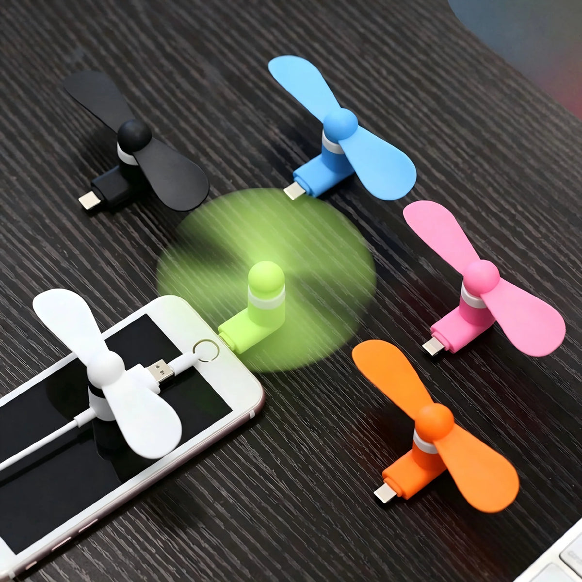 A collection of portable mini fans with soft blades in various colors including black, blue, pink, and orange, displayed on a
