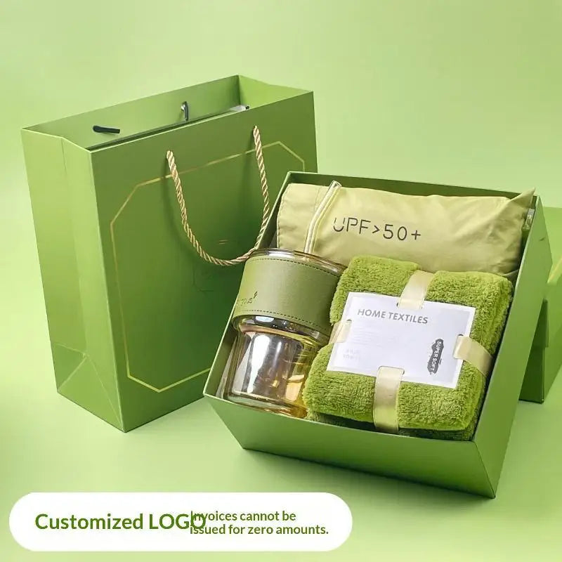 A green gift box contains a glass tumbler, a towel, and a sun protection item.