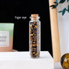 A glass bottle filled with tiger eye crystals, displayed on a white surface.