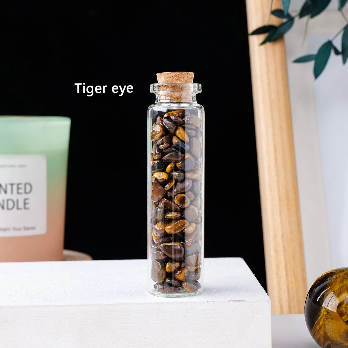 A glass bottle filled with tiger eye crystals, displayed on a white surface.