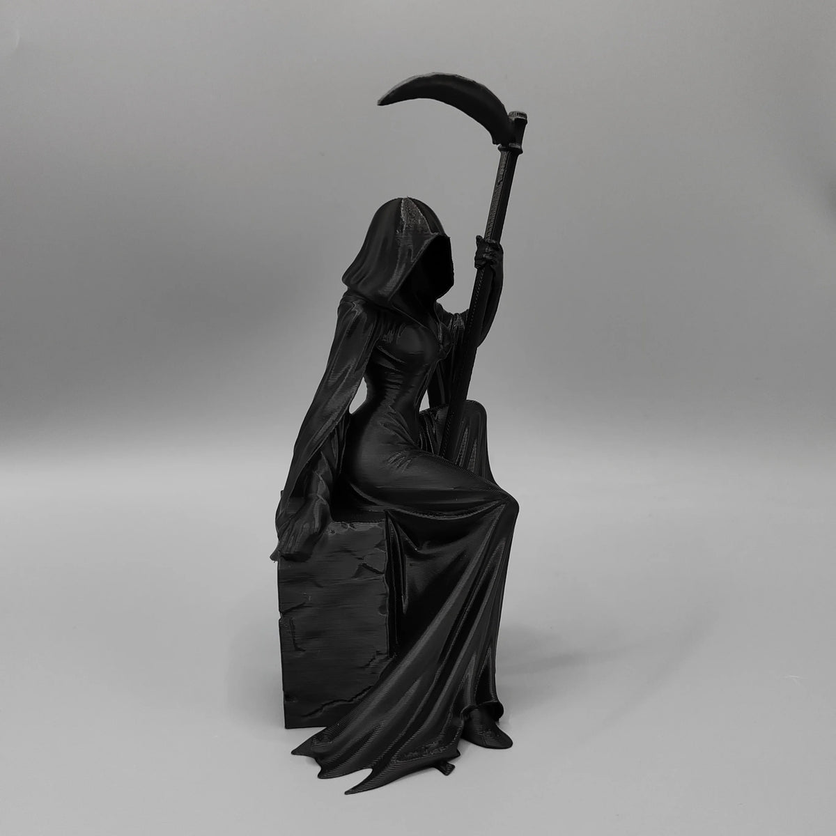 A black figurine of a gothic female grim reaper holding a large scythe.