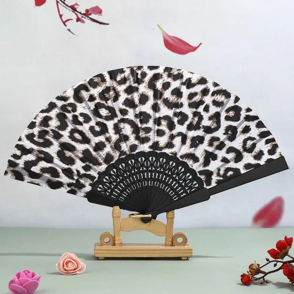 A leopard print folding hand fan with a black handle displayed against a light background.