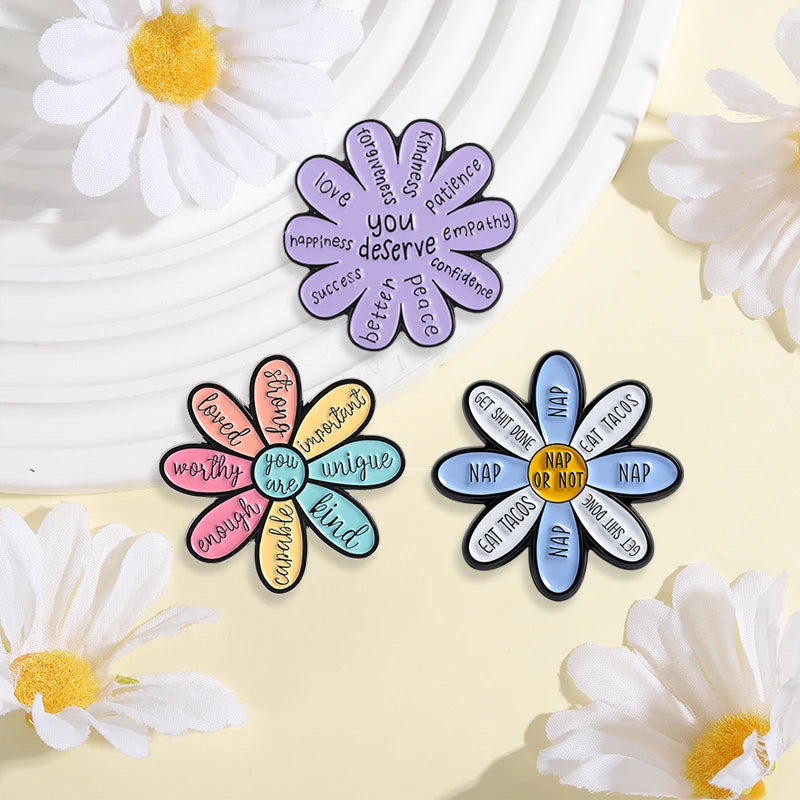 A set of enamel pins featuring cartoon cat and daisy flower designs with positive affirmations.