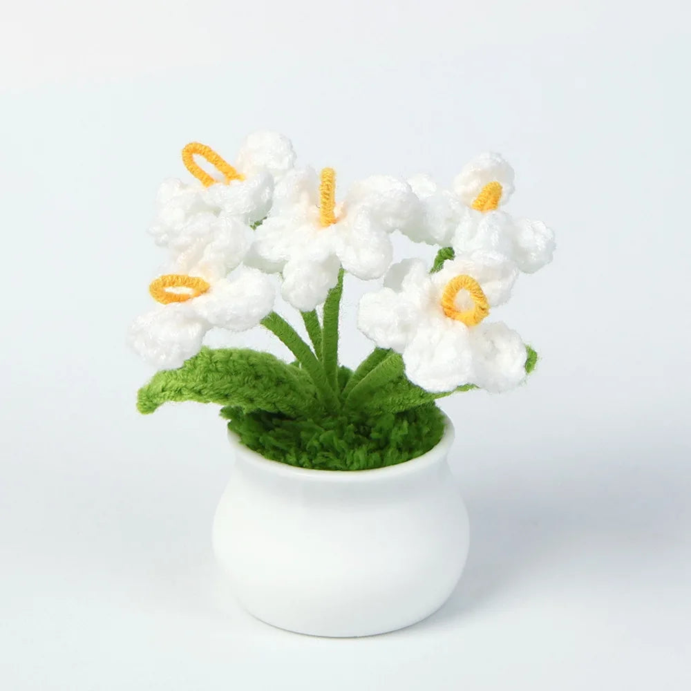 A cluster of white hand-woven crochet flowers with orange centers in a green potted plant.
