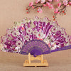 A purple and pink silk flower folding fan displayed on a wooden stand.
