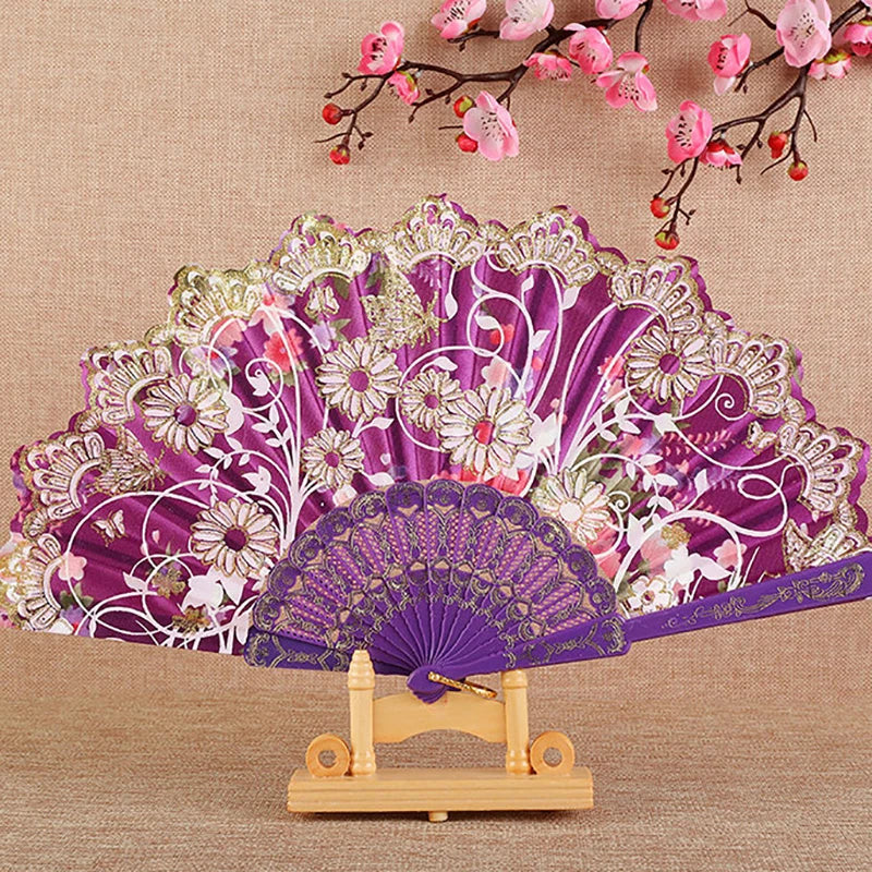 A purple and pink silk flower folding fan displayed on a wooden stand.