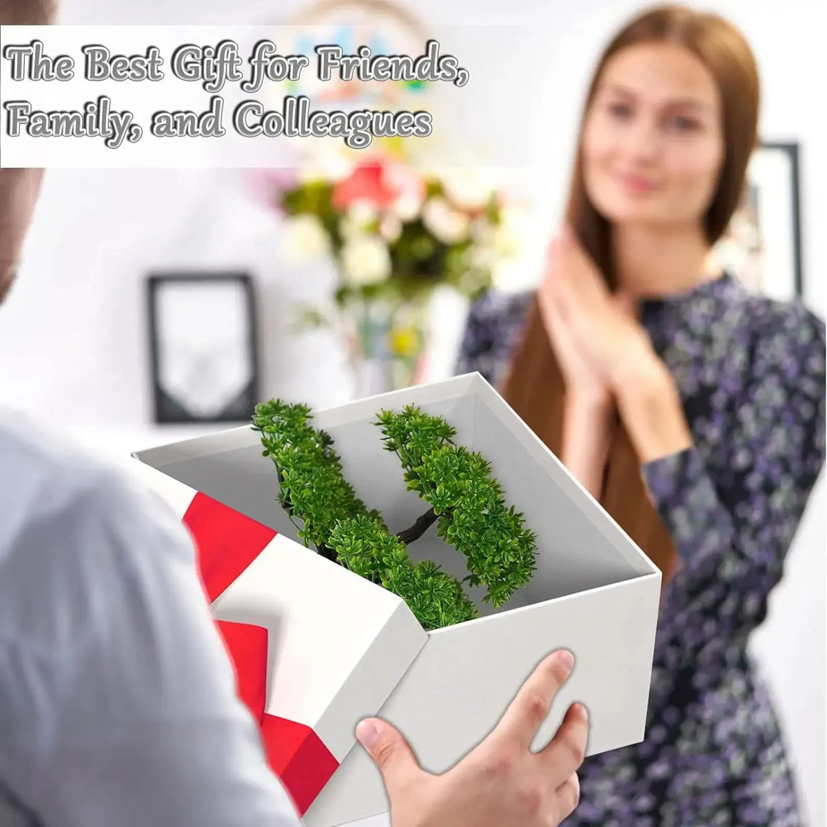 A person is holding an open white box containing artificial green bonsai trees for gift purposes.