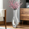 A tall silver mirrored vase with a crushed diamond finish holds pink cherry blossoms on a wooden cabinet.