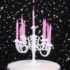 A white cake stand holds a decorative candelabra with nine pink striped birthday candles against a dark background of gold st