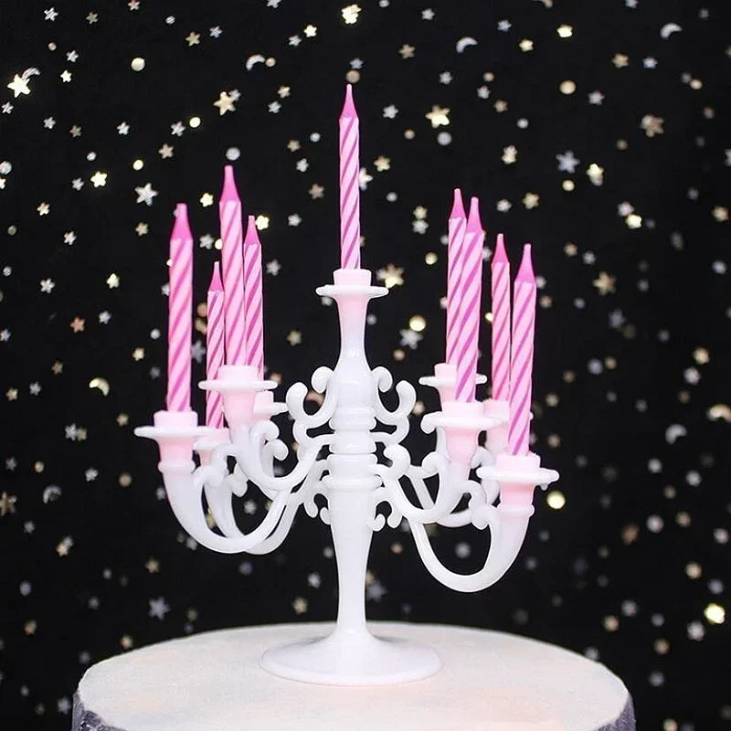 A white cake stand holds a decorative candelabra with nine pink striped birthday candles against a dark background of gold st