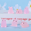 Pink glow-in-the-dark mini pig figurines displayed on a white surface with white flowers in the background.
