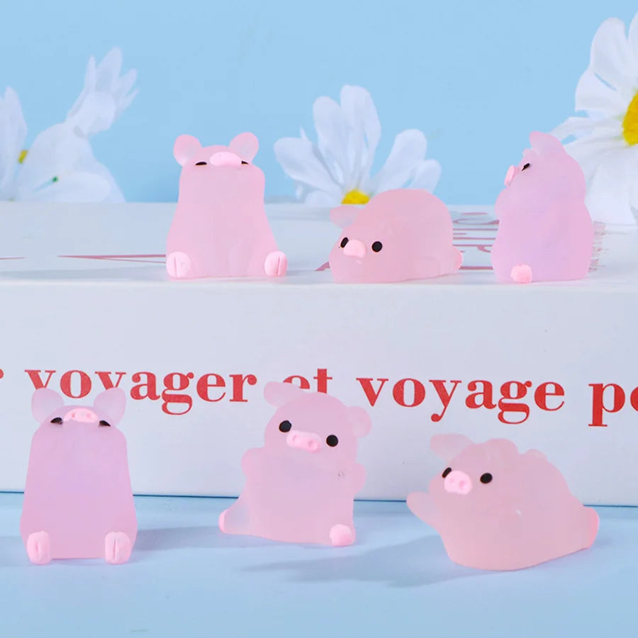 Pink glow-in-the-dark mini pig figurines displayed on a white surface with white flowers in the background.