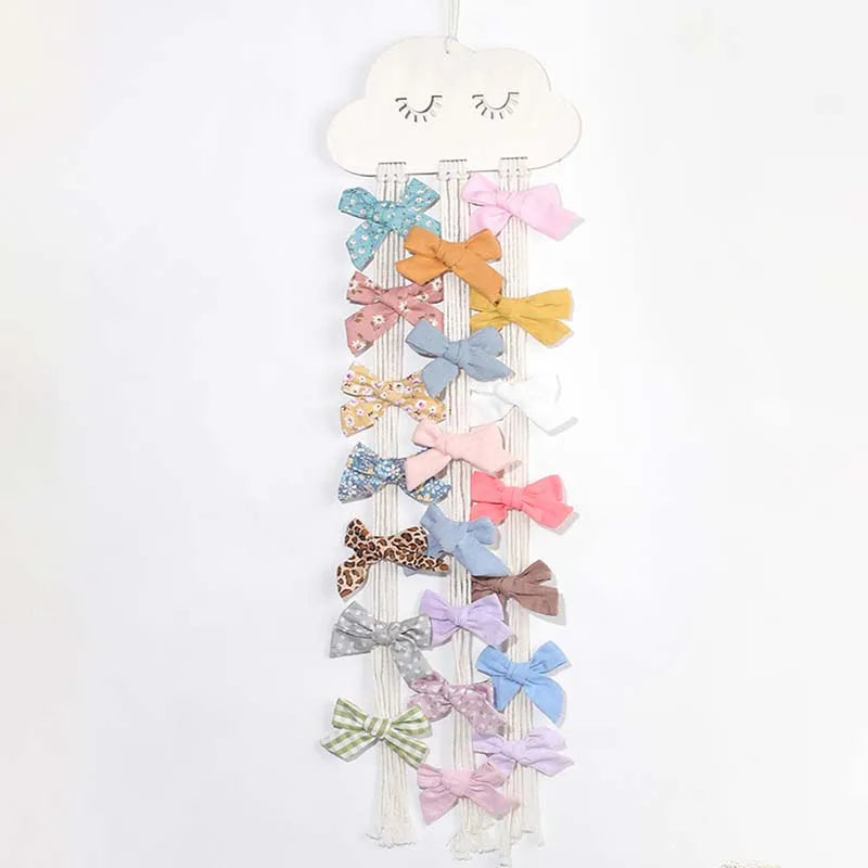 Wall-mounted headband holder with various pink and yellow fabric bows hanging from a cloud shape