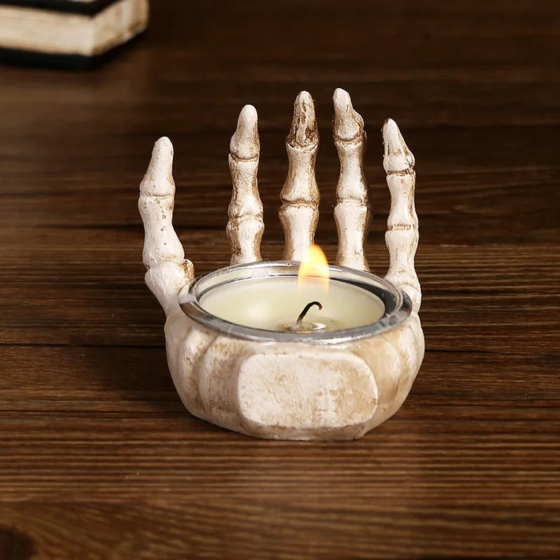 A white resin skull candle holder decoration with finger-like protrusions is placed on a dark wooden surface.