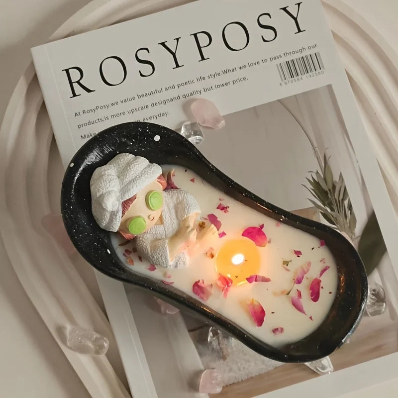 A white candle in a black silicone mold resting on a wooden surface with pink petals and a product label.