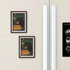 A framed print featuring a black cat looking at a slice of pizza, displayed on a light-colored wall.