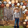 A young boy stands in front of a rustic wooden barn door backdrop decorated with various earth tones and black and white polk