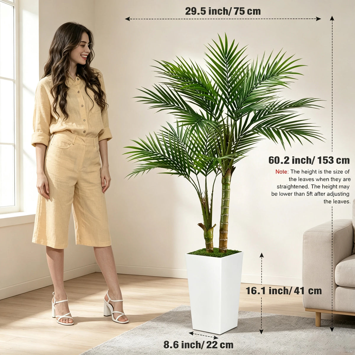 A woman stands next to a large artificial areca palm tree in a white pot, showcasing the plant's height and scale.