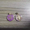 A pair of purple and silver religious pendants featuring the St. Benedict symbol and a depiction of the Virgin Mary.