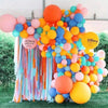 A vibrant balloon arch display featuring pastel colors like orange, yellow, pink, and blue, decorated with paper streamers.