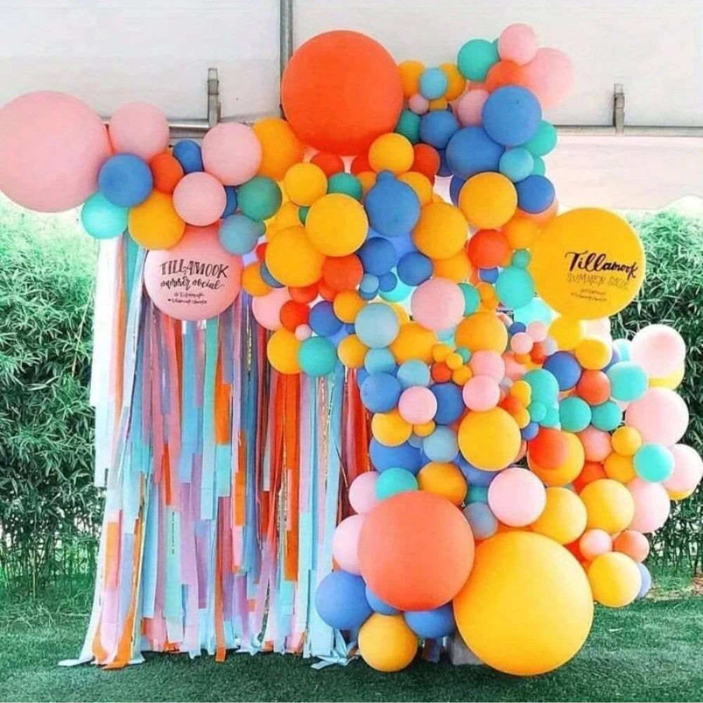 A vibrant balloon arch display featuring pastel colors like orange, yellow, pink, and blue, decorated with paper streamers.