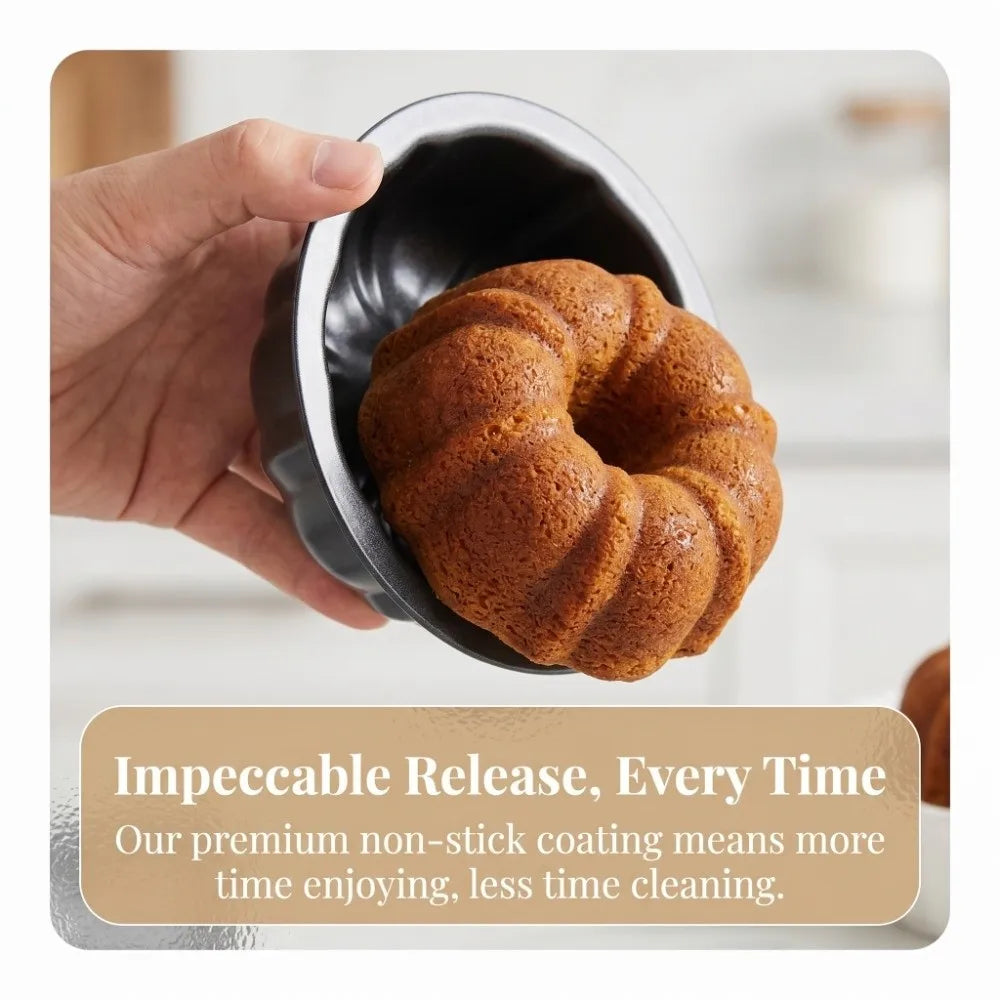A hand holds a dark nonstick mini fluted cake pan filled with baked cake.