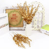 Golden artificial eucalyptus leaves arranged in a white vase against a rustic wooden frame and white door backdrop.