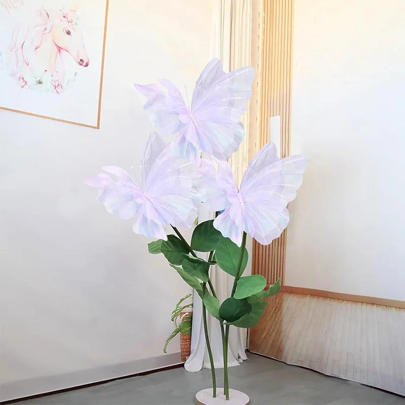 White silk artificial butterfly decoration with green leaves displayed against a light wall.