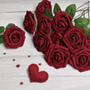A cluster of deep red velvet foam rose flowers with green stems on a white wooden surface.