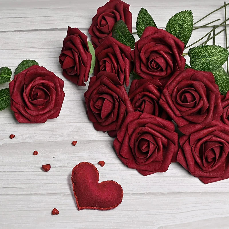 A cluster of deep red velvet rose flowers with green leaves and stems on a white wooden surface.