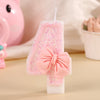 A pink bowknot birthday candle in a rectangular shape with glitter and a pink bow, set against a light background.