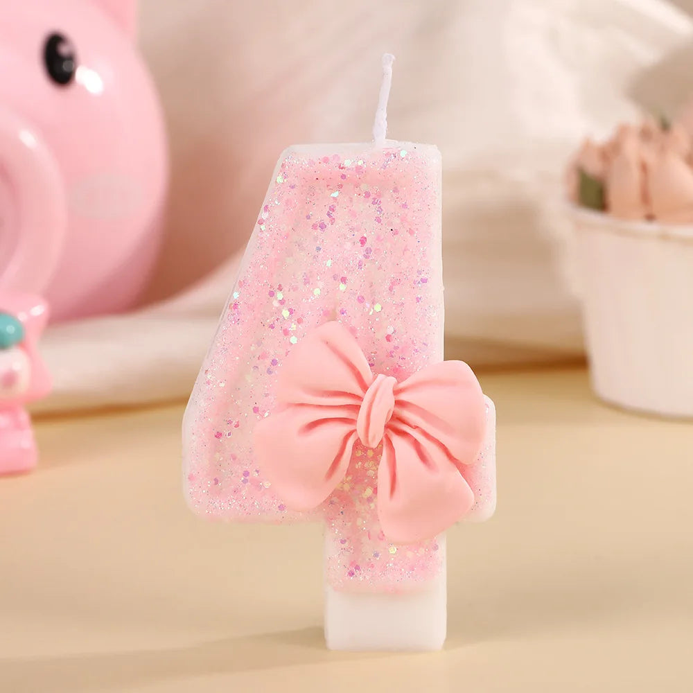 A pink bowknot birthday candle in a rectangular shape with glitter and a pink bow, set against a light background.