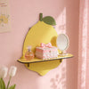 A yellow ceramic apple wall shelf featuring a pink box, perfume bottle, and a small mirror on a pink wall.