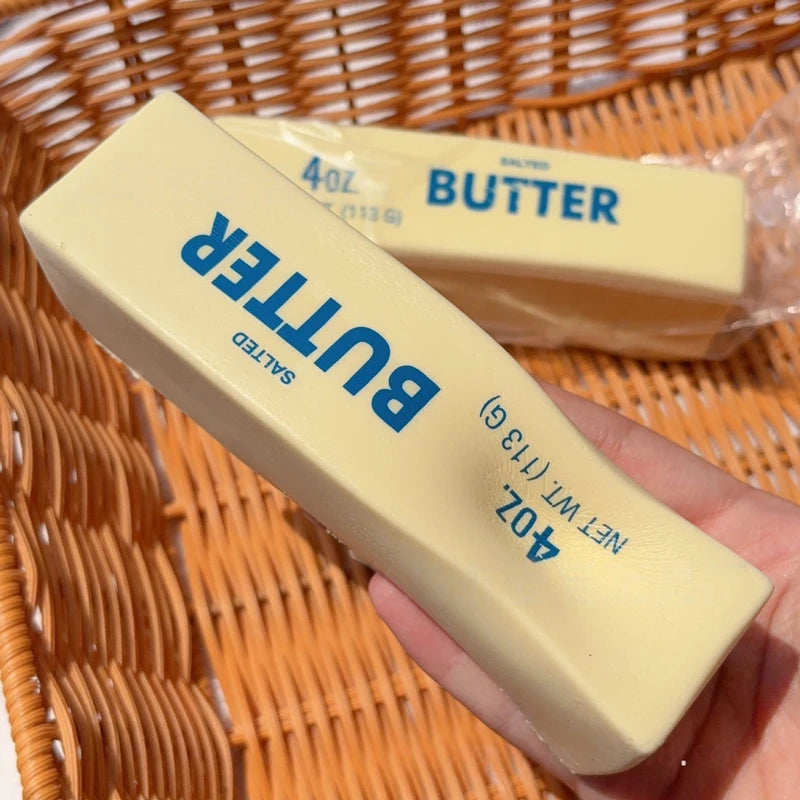A hand holds a yellow butter squeeze toy labeled Butter 4oz salted in a woven basket.