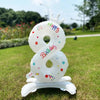 A white foil balloon shaped like the number 8 with a crown and birthday text, standing on green grass.