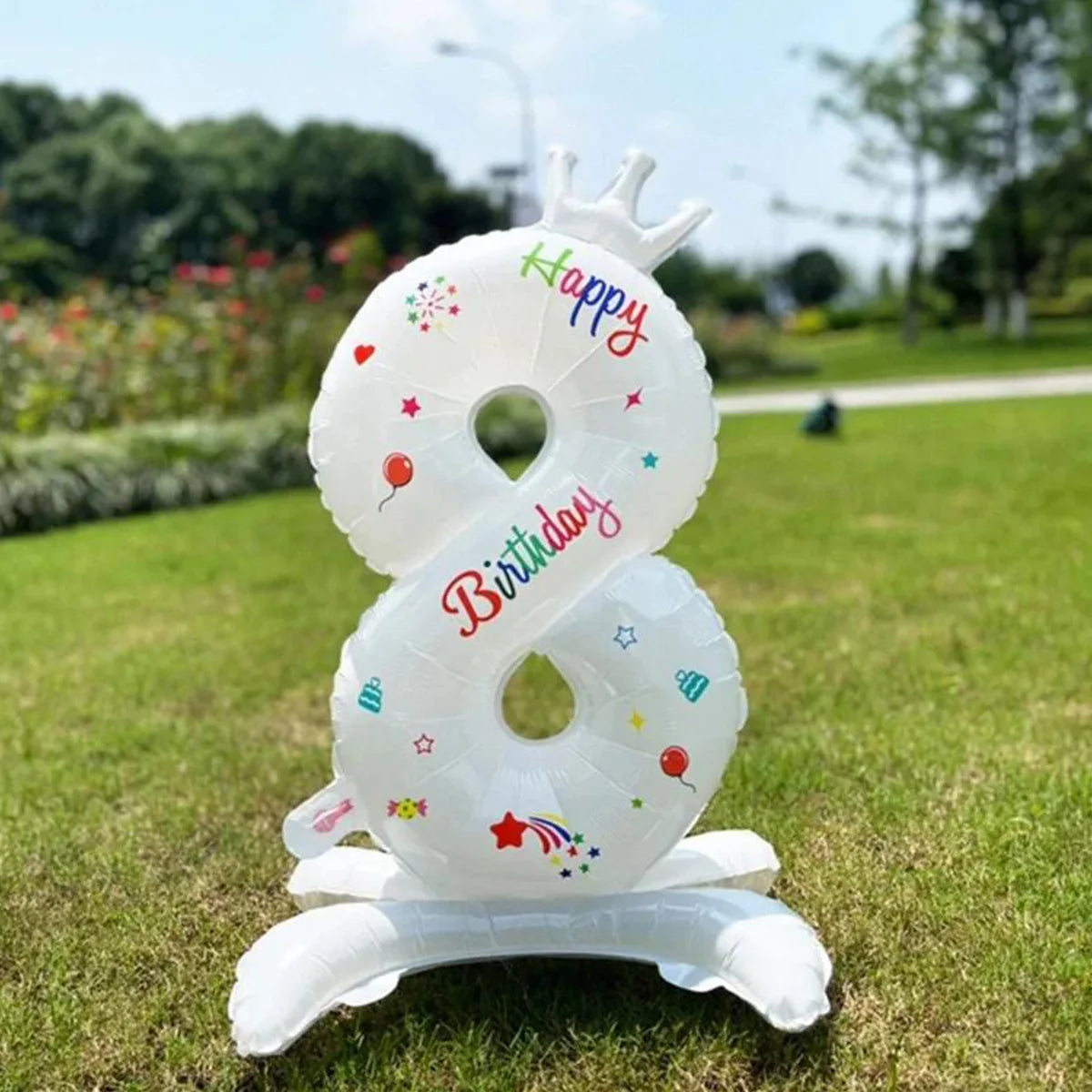 A white foil balloon shaped like the number 8 with a crown and birthday text, standing on green grass.