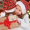 A young girl in a white sweater is smiling while holding a gift box tied with a red ribbon and a birthday tag.