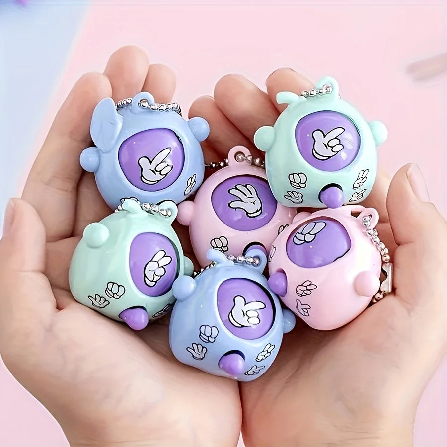 A hand holds several pastel colored mini rock-paper-scissors shaped keychains.