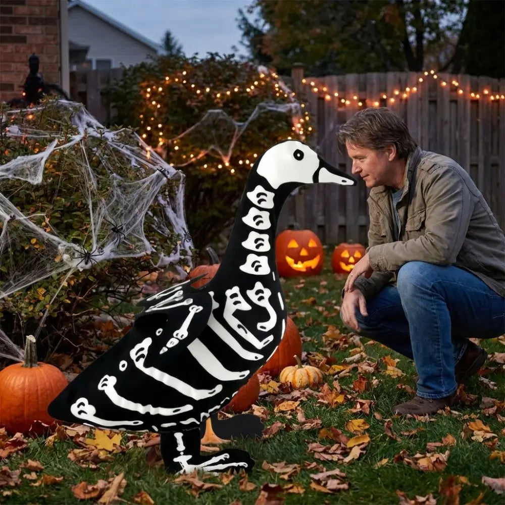 A man sits in a yard surrounded by autumn foliage and glowing lights, next to a black goose lawn decor with white skeleton pa