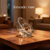 A clear glass vase holding an avocado seed on a wooden table.