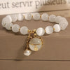 A white natural stone lily of the valley bracelet with gold accents displayed on a wooden surface.