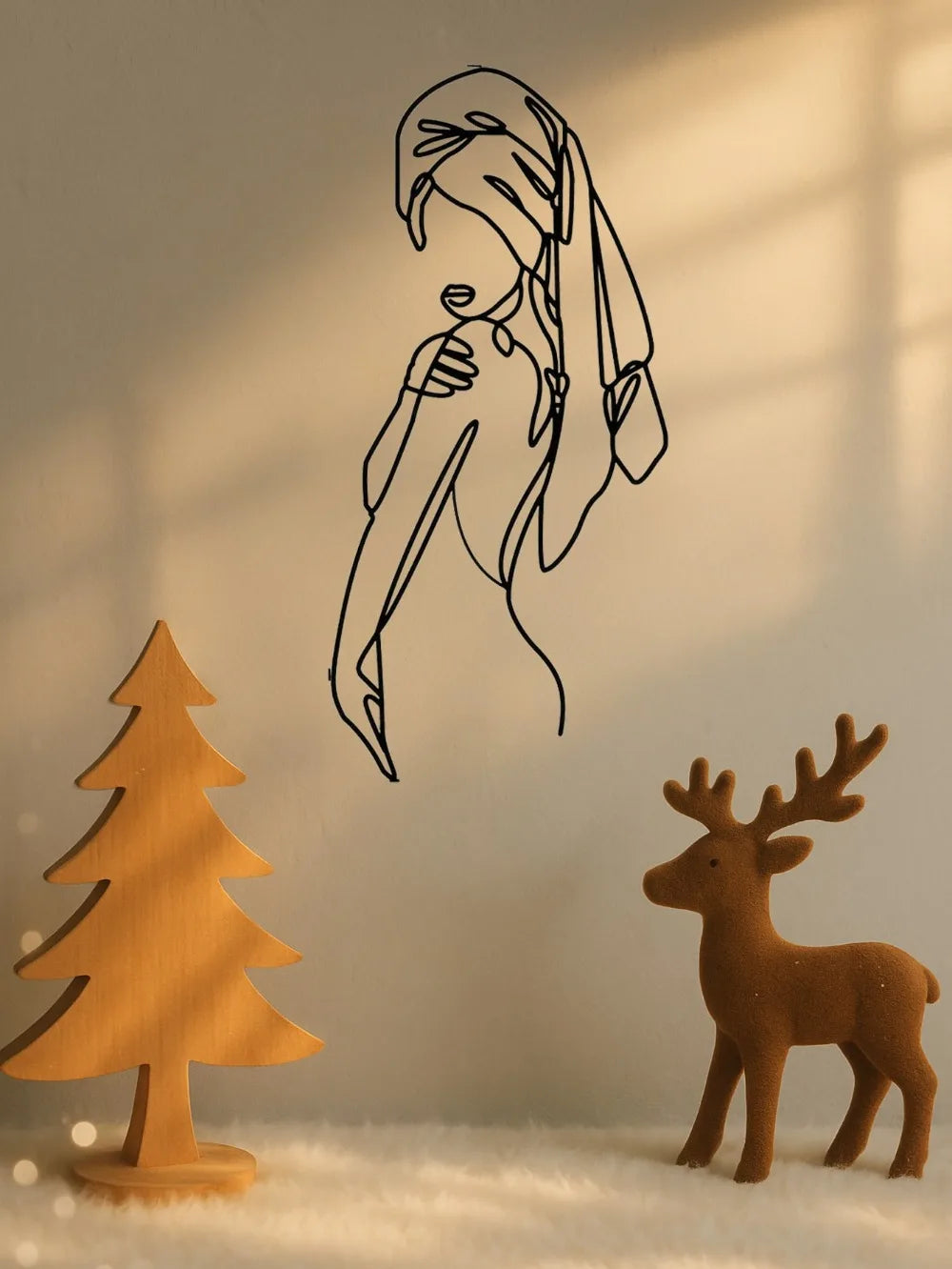 A black line art silhouette of a woman's profile on a wall, next to a wooden Christmas tree and a fawn.