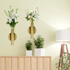 Minimalist wall-mounted metal flower vase with white flowers displayed on a light green wall.