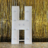 A large white marquee light-up letter H displayed against a shimmering gold curtain backdrop.