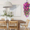 A vibrant purple morning glory and eucalyptus garland hangs on a wall above a wooden dining table.